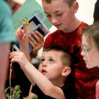 Group of students and young guest looking at a plant.